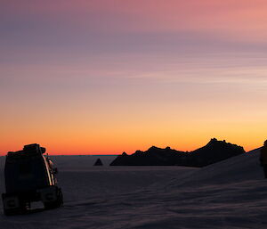 Outline of a Hagg and expeditioner standing on the snow with sunrise in the background