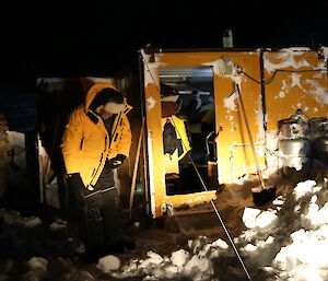 Colbeck Hut is yellow and lit by torches and headlights at night