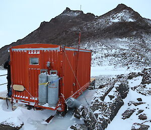 Henderson Hut is a red container shed against a rocky landscape.