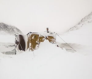 Colbeck Hut completely covered in snow and ice except for the roof and the door.