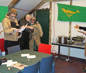 Four expeditioners study the menu while the chef points to the buffet and explains the dishes.