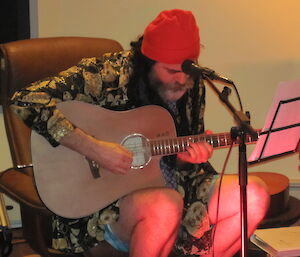 Man wearing a red beanie sitting and playing guitar.