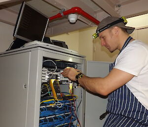 Justin wearing a chef’s apron and fiddling with wires while wearing ahead torch.