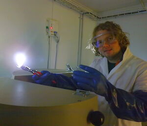 Keldyn Francis wearing safety goggles, gloves and white lab coat at a tank.