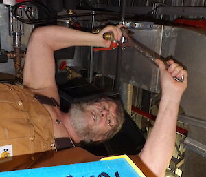 Lloyd Fletcher lying on the ground with a spanner wearing overalls.