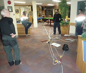 Two men laying out ropes on the ground inside a big room.