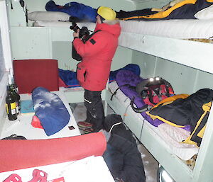 Clearing snow in hut that has sleeping bags and and clothes over the bunks.