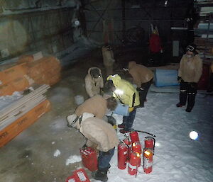 People in an old fire hangar working with red fire extinguisher bottles