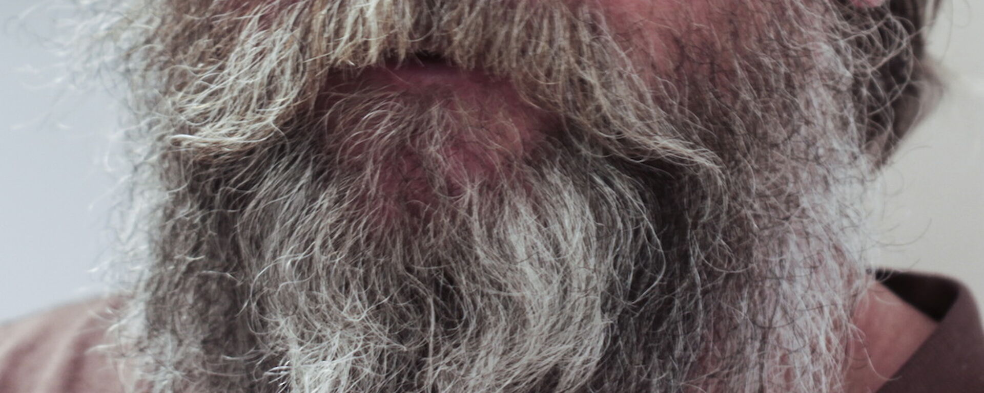 Photo of a man’s face form the nose down with a white and grey-haired beard.