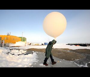 An expediitoner in a green coat holds a huge meteorology balloon release