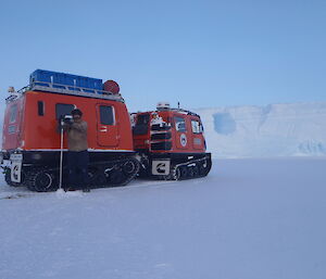 Man uding a long auger to drill standing beside a red Hagg vehicle