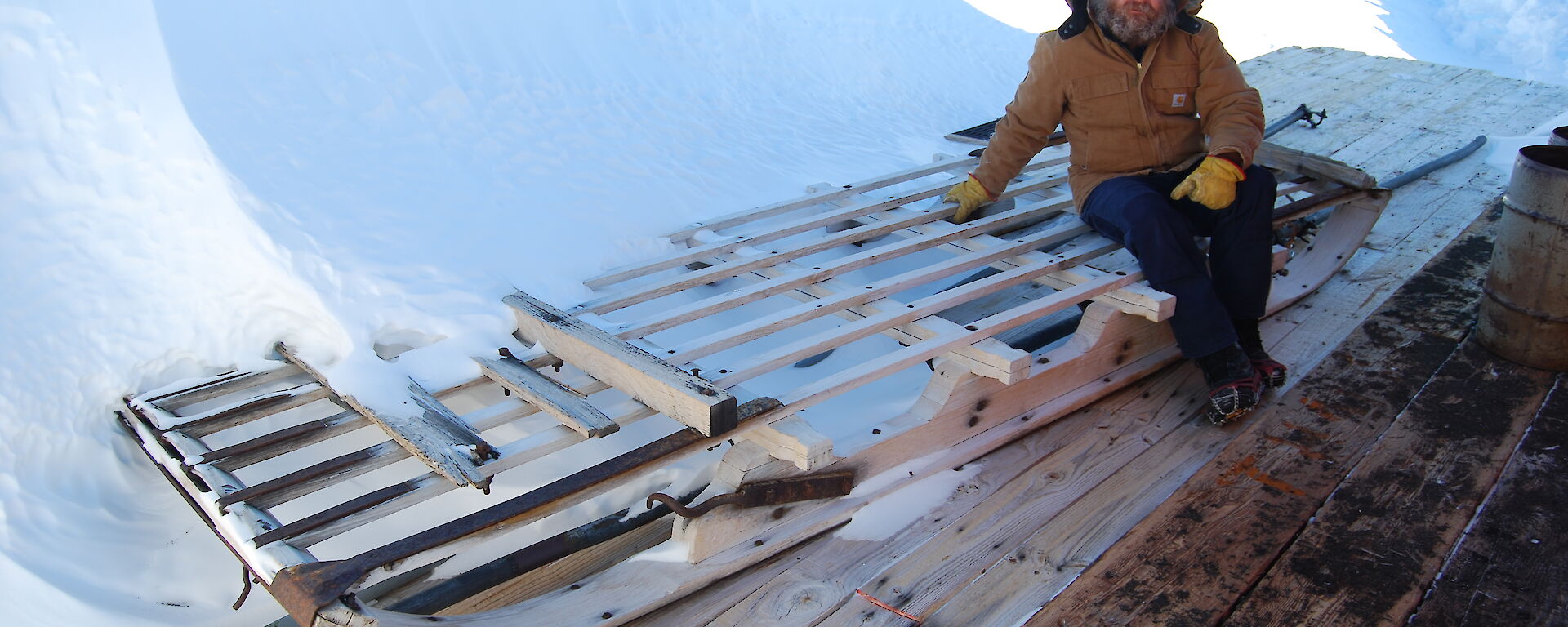 Expeditioner sitting beside a long wooden sledge