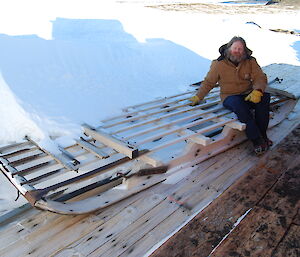 Expeditioner sitting beside a long wooden sledge