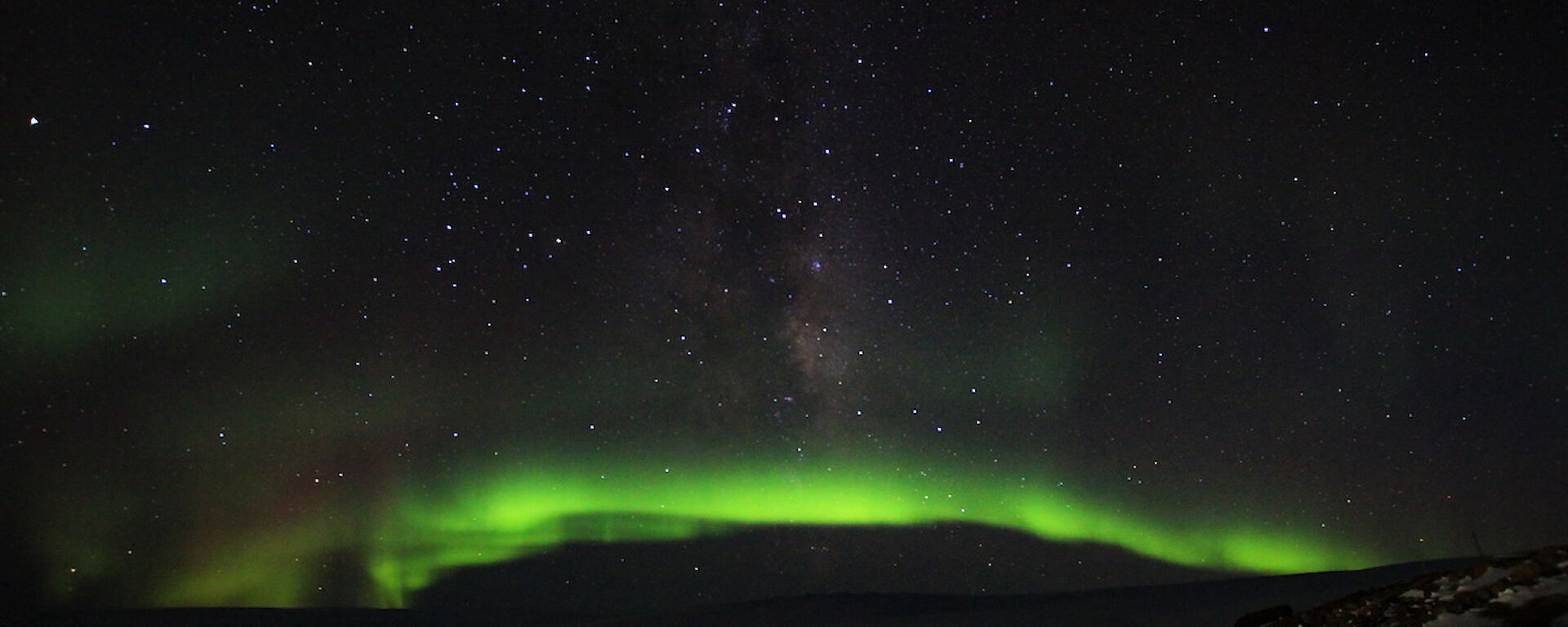 The aurora makes a bright green arc in the night sky over the station.