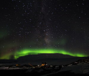 The aurora makes a bright green arc in the night sky over the station.