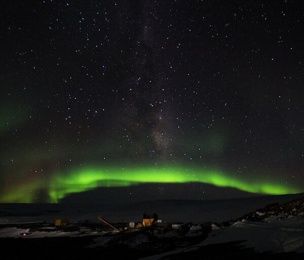The aurora makes a bright green arc in the night sky over the station.