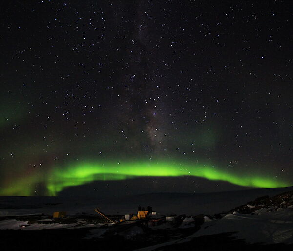 The aurora makes a bright green arc in the night sky over the station.