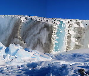 A dirty berg has dark sripes among the bright blue of the berg.