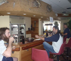 Expeditioners sitting at a bar sipping from glasses.