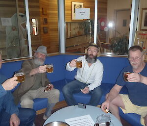Four men sitting on a blue lounge raise their glasses.