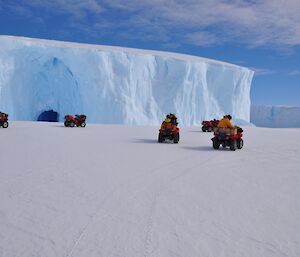 Exeditioners on quads driving past an ice cave in berg