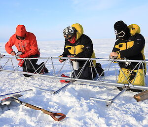 Three people lined up and securing pieces of the Auto weather station frame.