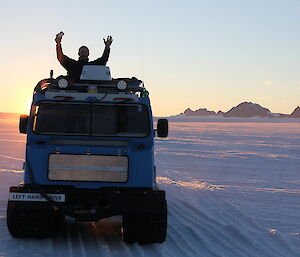 Male expeditioners stands up inside Hägglunds with sunset behind