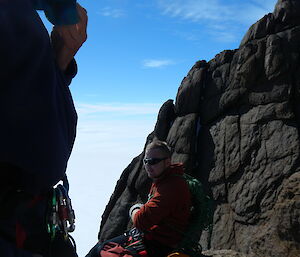 Expeditioner sitting in the rocks on a belay stop near Fang Peak