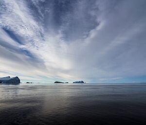 High cloud streak across the sky while the water below is still and calm.