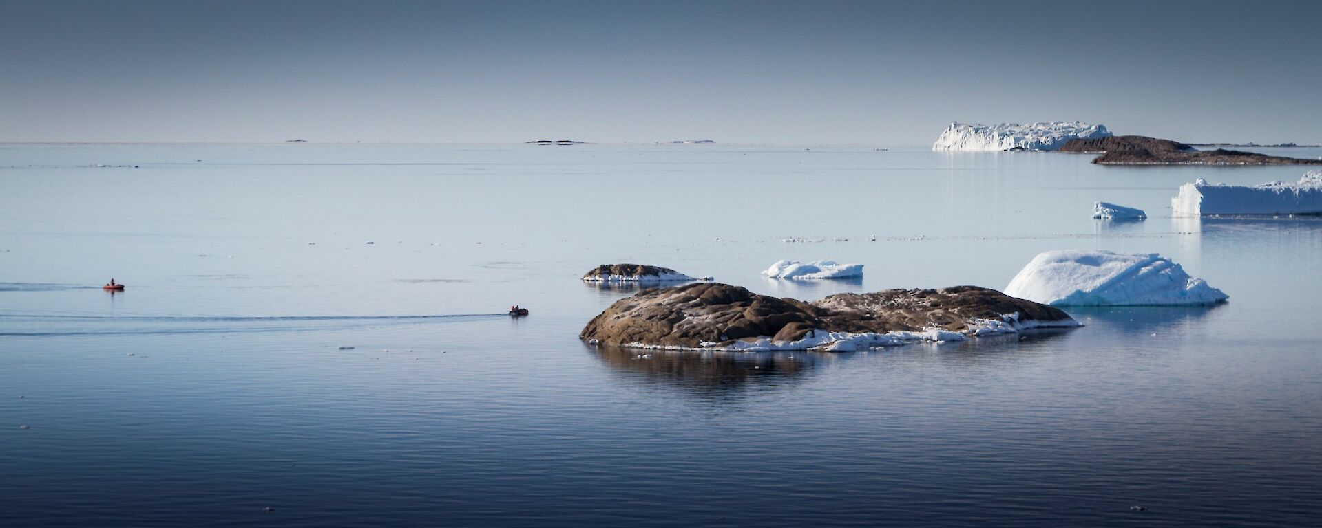 White bergs floating in glassy calm water.