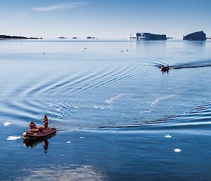 Two small boats streaking across the still sunny waters amongst the ice bergs.