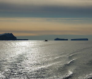 A sunset shot of expeditioners in a small rubber boat some distance from the camera, flanked by icebergs