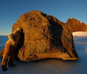 An expeditioner puts his ear up to a large jagged boulder jutting out from the ice