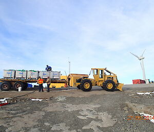 A tractor and large flat try with fuel pods is prepared by three expeditioners to pump fuel