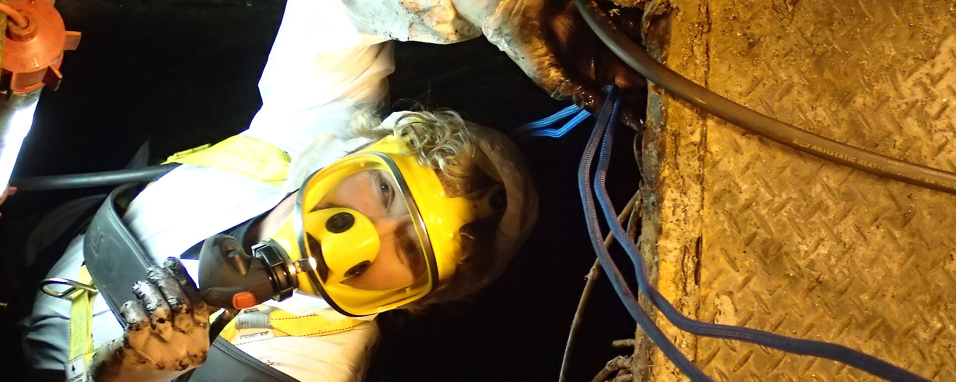 A plumber works in a confined space with a protective mask and oxygen for breathing