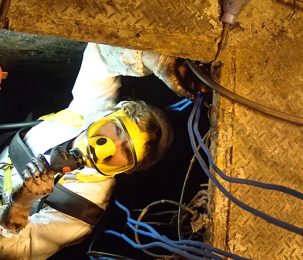 A plumber works in a confined space with a protective mask and oxygen for breathing