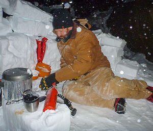 Expeditioner sitting beside a camp stove and shielded by a wall of snow blocks
