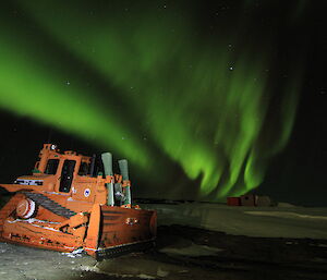 Aurora australis lights in the sky over a dozer parked at Mawson station