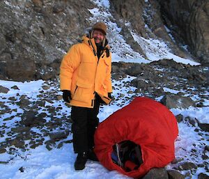 Expeditioner standing next to his bivvy bag which is filled with his survival gear