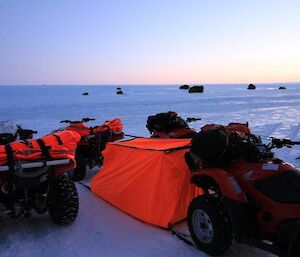 A bright orange quad bivvy stretched between two Quad Motorbikes