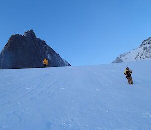 Two expeditioners standing on an ice slope with ice axes in hand preparing to practise self arresting