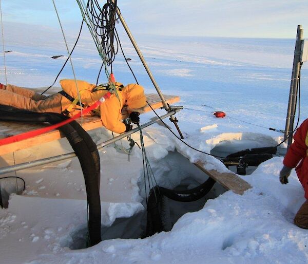 A tradesman lying on the deck of the melt bell as he holds the suspended pipe work