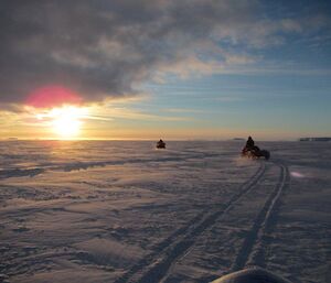 Expeditioners riding their quad motorbikes on the sea ice toward the setting sun