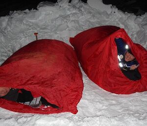 Two expeditioners lying in their bivvy bags in the snow
