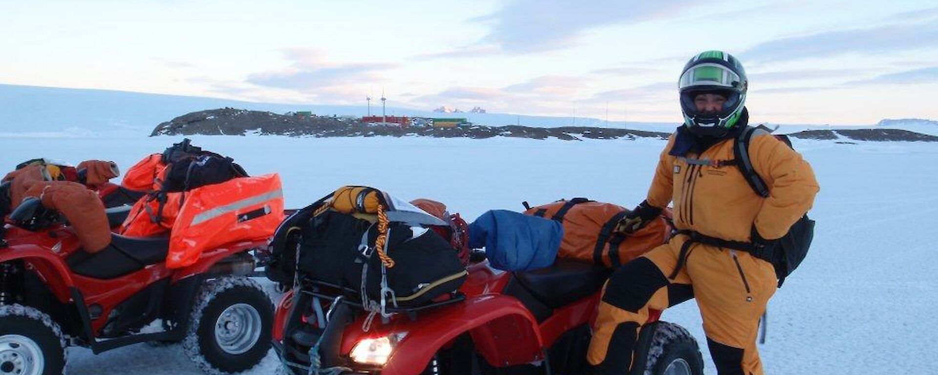 an expeditioner standing beside her quad bike with Mawson Station in the background