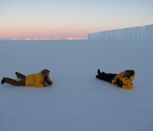 Two expeditioners lying on the sea ice waiting for the next troupe of emperor penguins to wander by