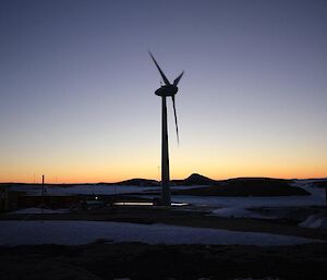 A wind turbine with the sun rising in the background