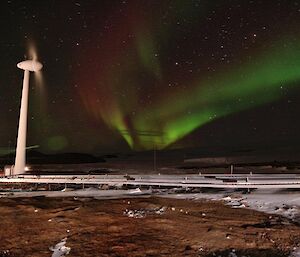 An Aurora towering above a wind turbine at night