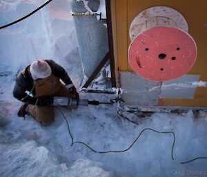 An expeditioner removes ice from beneath the hut with a jackhammer