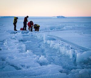 Expeditioners drilling the sea ice at a tide crack